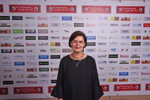 Portrait einer Person vor einer Sponsorwand mit vielen Firmenlogos, zentrale Person steht im Vordergrund für eine Veranstaltungsdokumentation.
