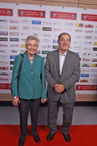 Zwei Personen stehen auf rotem Teppich vor einer Sponsorwand und posieren für ein offizielles Foto bei einer Veranstaltung.