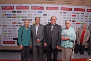 Vier Personen stehen nebeneinander für ein Gruppenfoto vor einer Sponsorwand mit Logos; Hintergrund dient zur Kontextgebung des Anlasses.