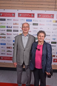 Zwei Personen stehen nebeneinander vor einer Sponsorwand mit Logos, beide blicken in die Kamera und posieren bei einer Veranstaltung.