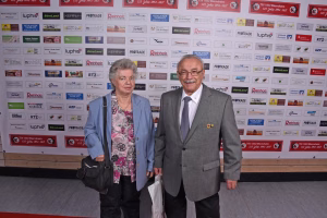 Zwei Personen stehen vor einer Sponsorwand und posieren für ein Foto bei einer Veranstaltung.