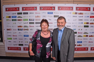 Zwei Personen stehen gemeinsam vor einer Sponsorwand; sie posieren frontal für ein Eventfoto, die Logos sind im Hintergrund sichtbar.