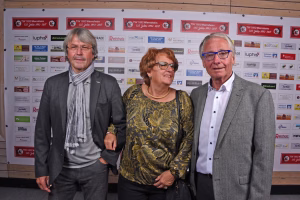 Drei Personen posieren gemeinsam vor einer Sponsorwand, als Porträt bei einer Veranstaltung zur Dokumentation der Beteiligten.