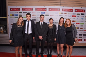 Sechs Personen in festlicher Kleidung posieren vor einer Sponsorwand; Gruppenfoto für einen offiziellen Anlass oder Wettbewerb.
