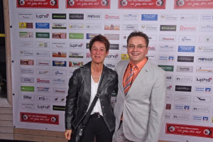 Zwei Personen lächeln vor einer Sponsorwand mit vielen Logos und Jahresbannern, stehen für ein Veranstaltungsfoto bereit.