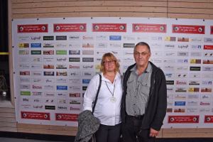 Zwei Personen vor einer Sponsorwand mit vielen Logos; Porträtaufnahme im Rahmen einer Veranstaltung.