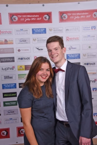 Zwei Personen posieren lächelnd vor einer Sponsorwand; Anzug und Kleid, Foto zur Darstellung eines offiziellen Anlasses und Promotion.