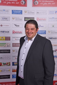 Grinsender Mann im Anzug vor einer Sponsorwand mit vielen Logos, Fotopose bei Veranstaltung/Preisverleihung.
