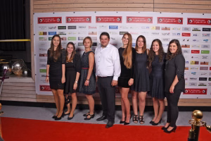 Personengruppe bei einer Veranstaltung vor einer Sponsorwand, posiert für ein Gruppenfoto; roter Teppich im Vordergrund.