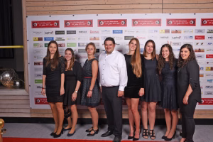 Gruppe von sieben Personen posiert auf rotem Teppich vor Sponsorenwand im Veranstaltungsbereich; Kamera auf Augenhöhe, Präsentationsfoto.