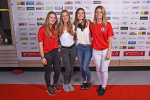 Vier junge Frauen stehen nebeneinander auf rotem Teppich vor bedruckter Sponsorenwand und lächeln in die Kamera.