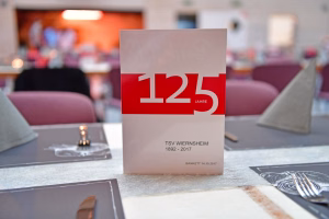 Festliches Tischdisplay mit rotem „125 Jahre“-Aufdruck und Datumsangaben, im Vordergrund bei gedeckter Veranstaltung.