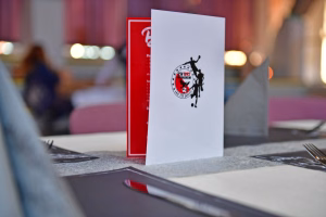 Auf einem Tisch steht eine rote und eine weiße Karte mit rundem Logo; durch unscharfen Hintergrund wirkt sie als Blickfang.