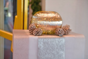 Goldfarbene Kugelvase mit feinen Lichtreflexen, auf einem Steinpodest und mit Tannenzapfen dekoriert.