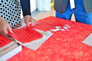 Hände sortieren rote Unterlagen mit gedruckten Textzeilen und Etiketten auf einem Tisch, vermutlich für Versand oder Archivierung.