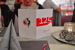 Jubiläumstüte mit „125 Jahre“-Aufdruck, daneben Karten und dekorative Tortenstücke auf einem Tisch bei einer Feier.