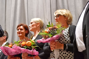 Mehrere Personen halten Blumensträuße mit buntem Beiwerk in rosa Geschenkpapier, im Vordergrund Übergabe und Gratulation bei einer Veranstaltung.
