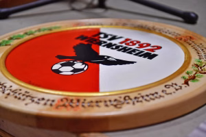 Ovales Spielbrett mit rotem und weißem Feld, Fußballsymbol und schwarz-weißer Aufschrift, um ein Motiv bzw. Spielthema zu zeigen.