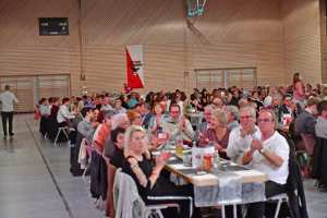 Festliche Tischreihen in einer Sporthalle mit vielen Besuchern; im Hintergrund stehen Flaggen und ein Banner als Anlassdekoration.