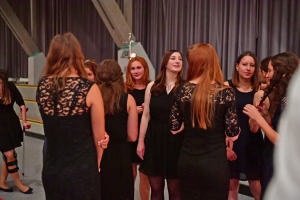 Gruppe von Frauen in dunklen Kleidern steht im Innenraum vor Vorhang und Publikum; Gespräche und gemeinsames Feiern.