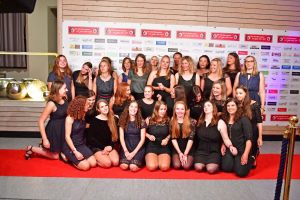 Gruppenfoto mehrerer Frauen in zwei Reihen auf rotem Teppich vor einer Sponsorwand, im Hintergrund ausgestellte Festdekoration.