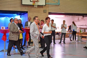 Mehrere Personen laufen im Innenraum einer Sporthalle zu Musik, während Zuschauer im Hintergrund warten; Tanzausdruck auf dem Boden.