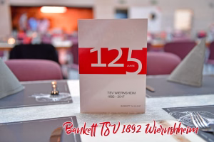 Stehende Jubiläums-Karte mit rotem „125“ und „JAHRE“, vor gedecktem Tisch mit Deko und unscharfem Hintergrund zur Begrüßung.