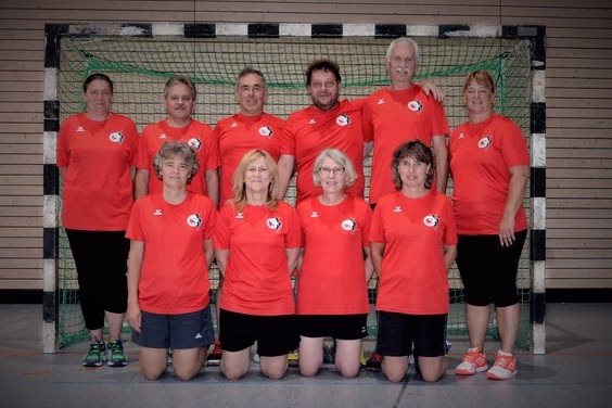 Mannschaftsgruppe in roten Trikots vor einem Fußballtor, zur Präsentation als Teamfoto in einer Sporthalle.