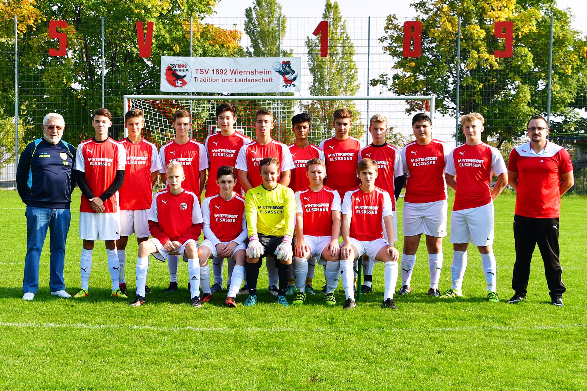 Mannschaftsfoto einer Jugendfußballmannschaft vor dem Tor auf dem Sportplatz, mit Trainer und Spielern in einheitlichen Trikots, im Hintergrund Banner.