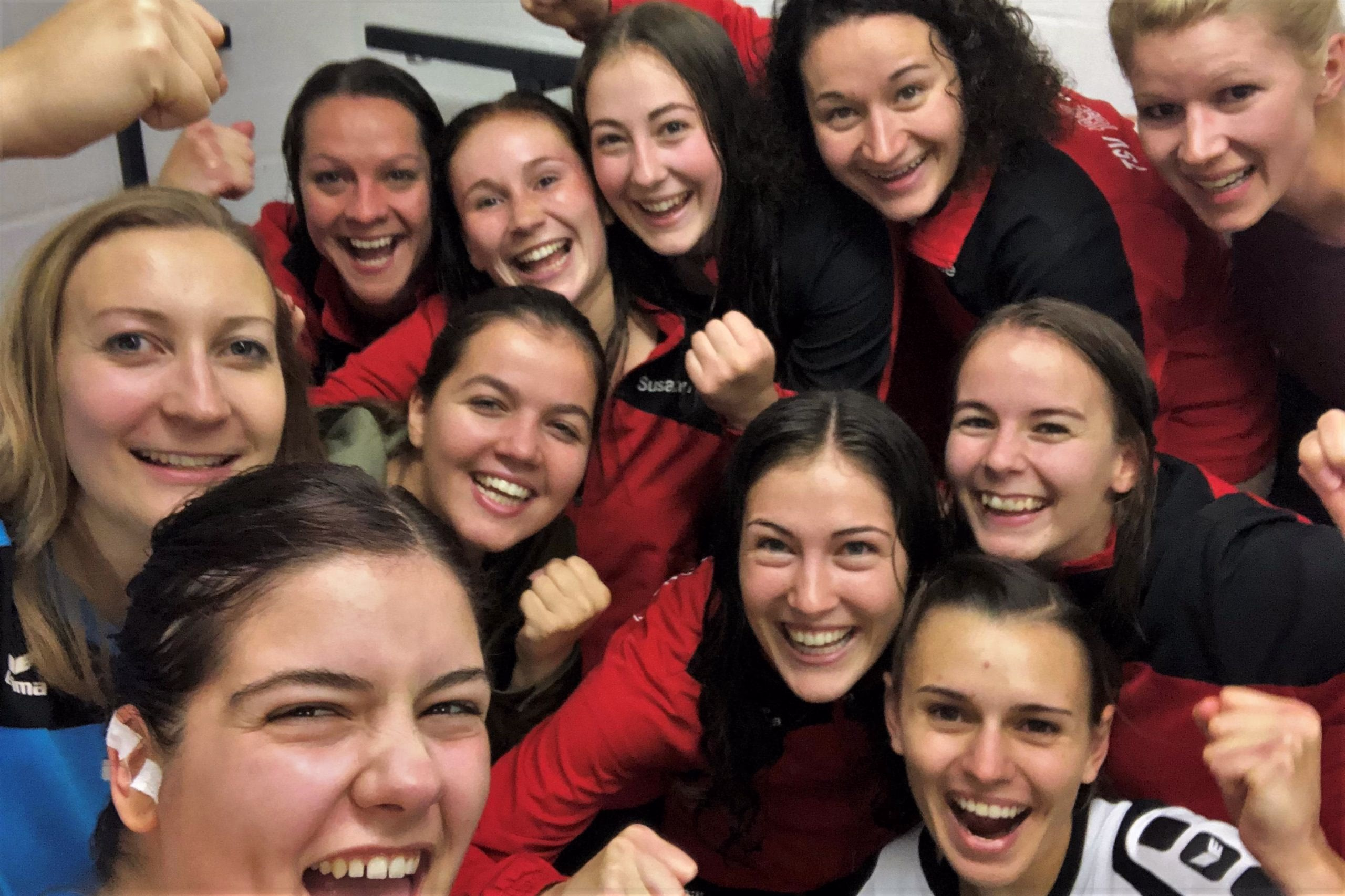 Gruppenselfie von mehreren lachenden Damen in roten Sportkleidern, dicht beieinander, leicht verwackelt, als Teamfoto.