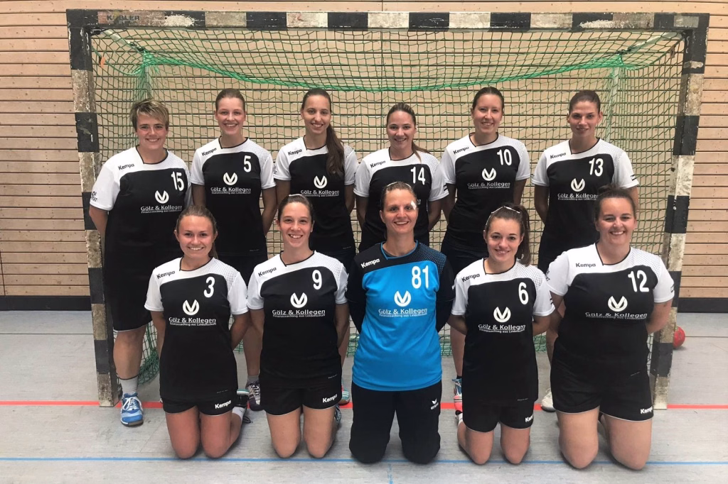 Damen II sichern sich knapp ihre ersten Punkte 2 Handballteam posiert vor dem Tor; mehrere Spielerinnen in Trikots mit Startnummern, eine Person kniet vorn.