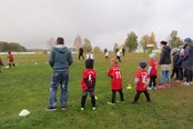 Freizeitgruppe steht auf Wiese; eine Person erklärt, Kinder beobachten und halten kleine Flaggen, gemeinsames Outdoorspiel mit Anleitung