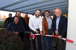 Gruppe bei der Terrasseneröffnung: mehrere Personen stehen vor überdachtem Bereich und durchschneiden mit rotem Band eine Absperrung.