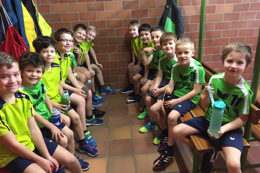 Mini-Handballer spielen in Illingen 8 Gruppe von Kindern im Sportdress sitzt auf einer Treppenstufe an der Backsteinwand, einige halten Getränkeflaschen und lächeln.