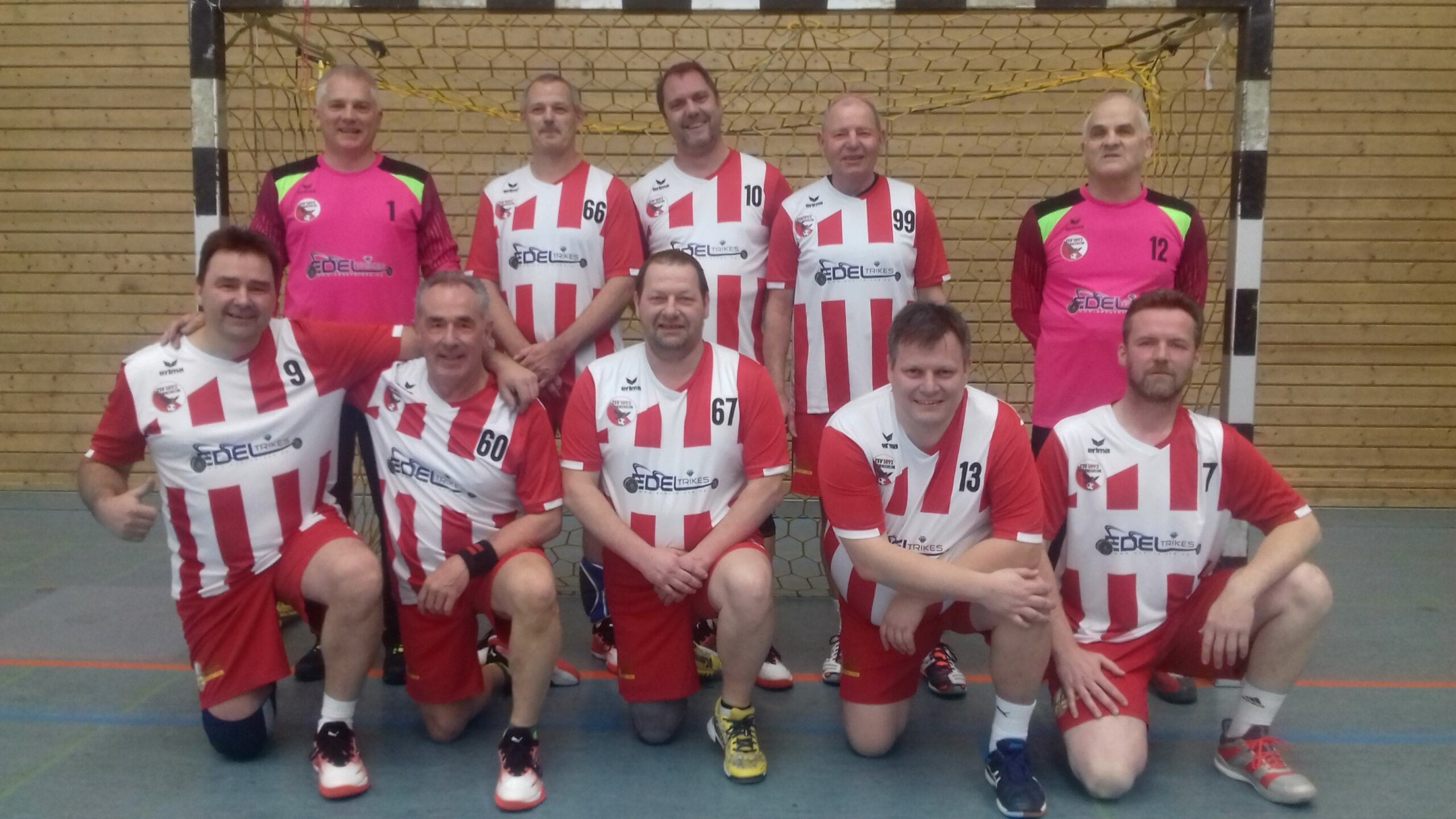 Mannschaftsbild mehrerer Handballspieler vor dem Tor, in Trikots posierend; Nummern sichtbar, Zweck: Teamdarstellung.