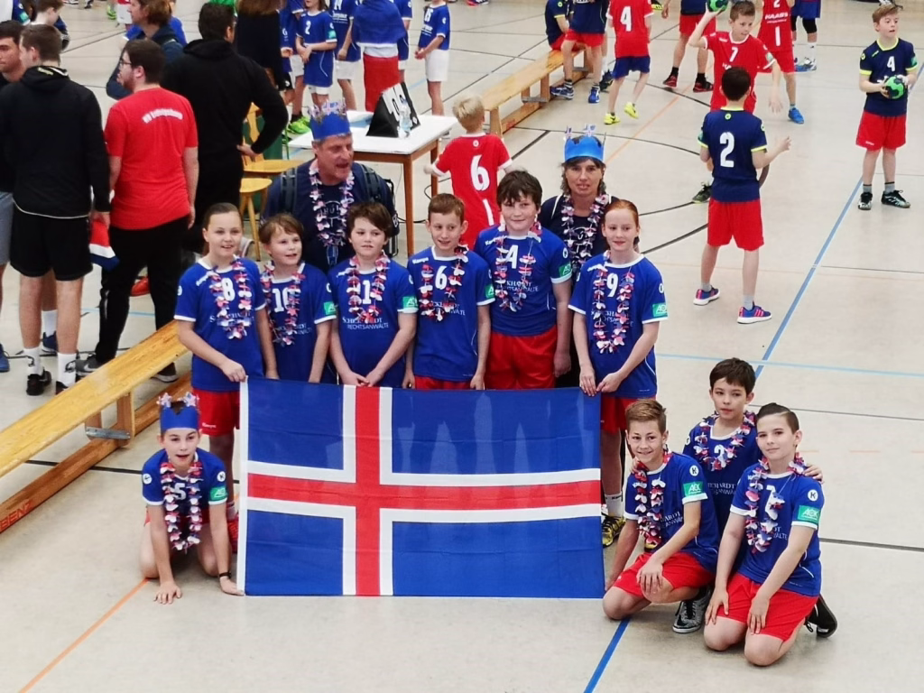 Fan-Preis bei der Mini-WM 2 Jugendliche Handballmannschaft posiert in Sporthalle vor großes finnisches Flaggenbanner. Trainer und Fans im Hintergrund.
