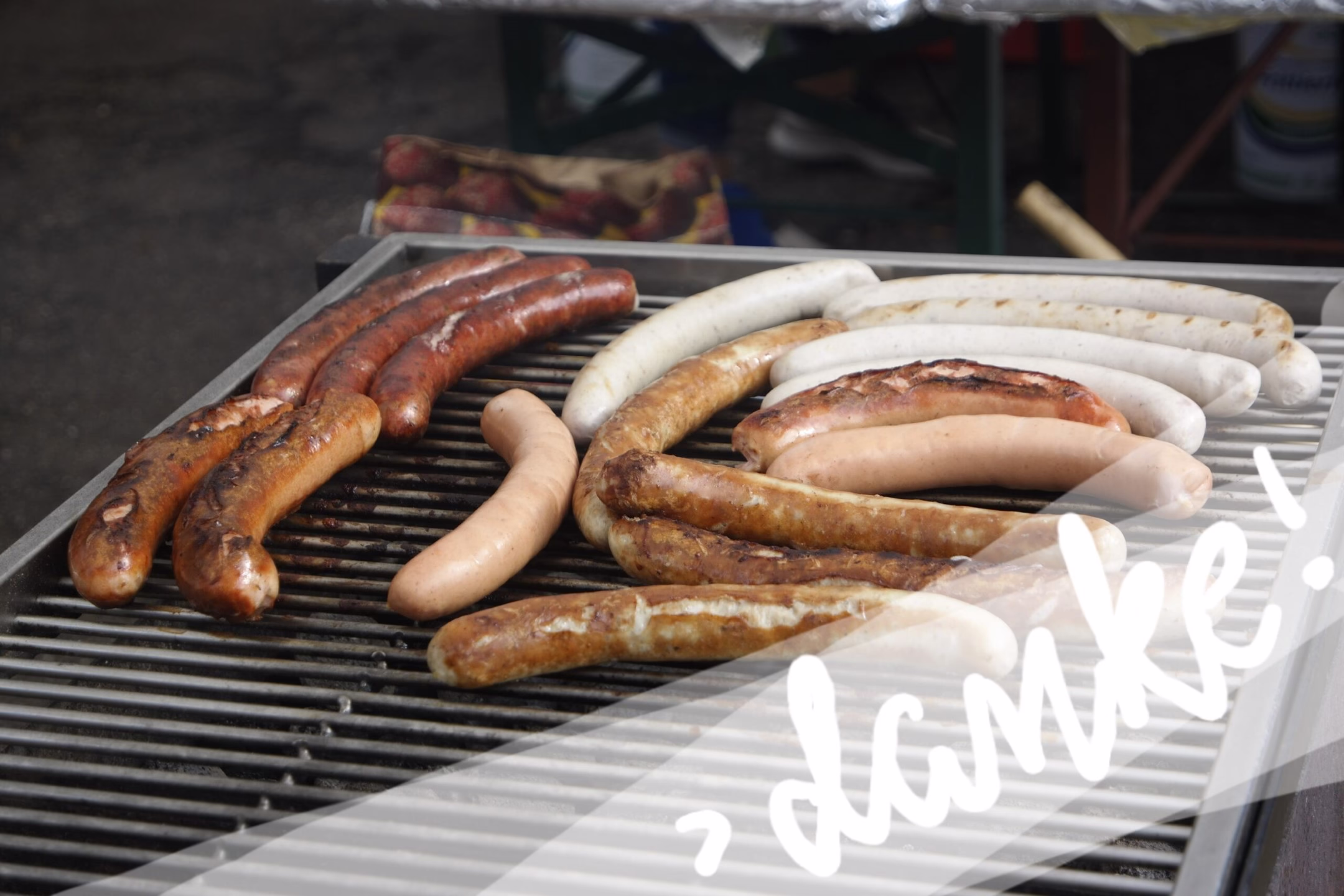 Gegrillte Würstchen auf einem Grillrost, mit sichtbarem Bratengrillgut und typischer Zubereitung beim Straßenfest.