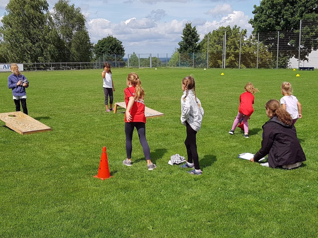 Ferienerlebnistag beim TSV Wiernsheim 5 Kinder stehen auf einem Rasen und üben Parcours mit Leitkegeln und Hürden, angeleitet im Sport-/Spieltraining.