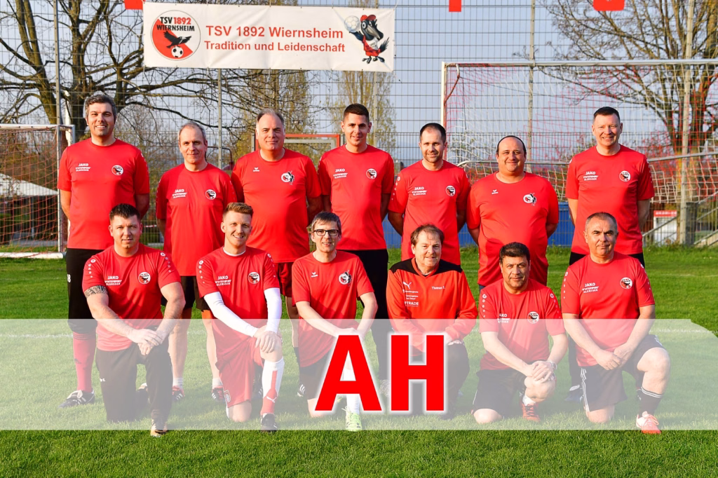 Kunstrasenplatzeinweihung SFG Serres 6 Mannschaftsbild auf Fußballplatz: elf Personen in roten Trikots stehen und knien vor Tor und Zaun, mit großem roten AH-Schriftzug im Vordergrund.