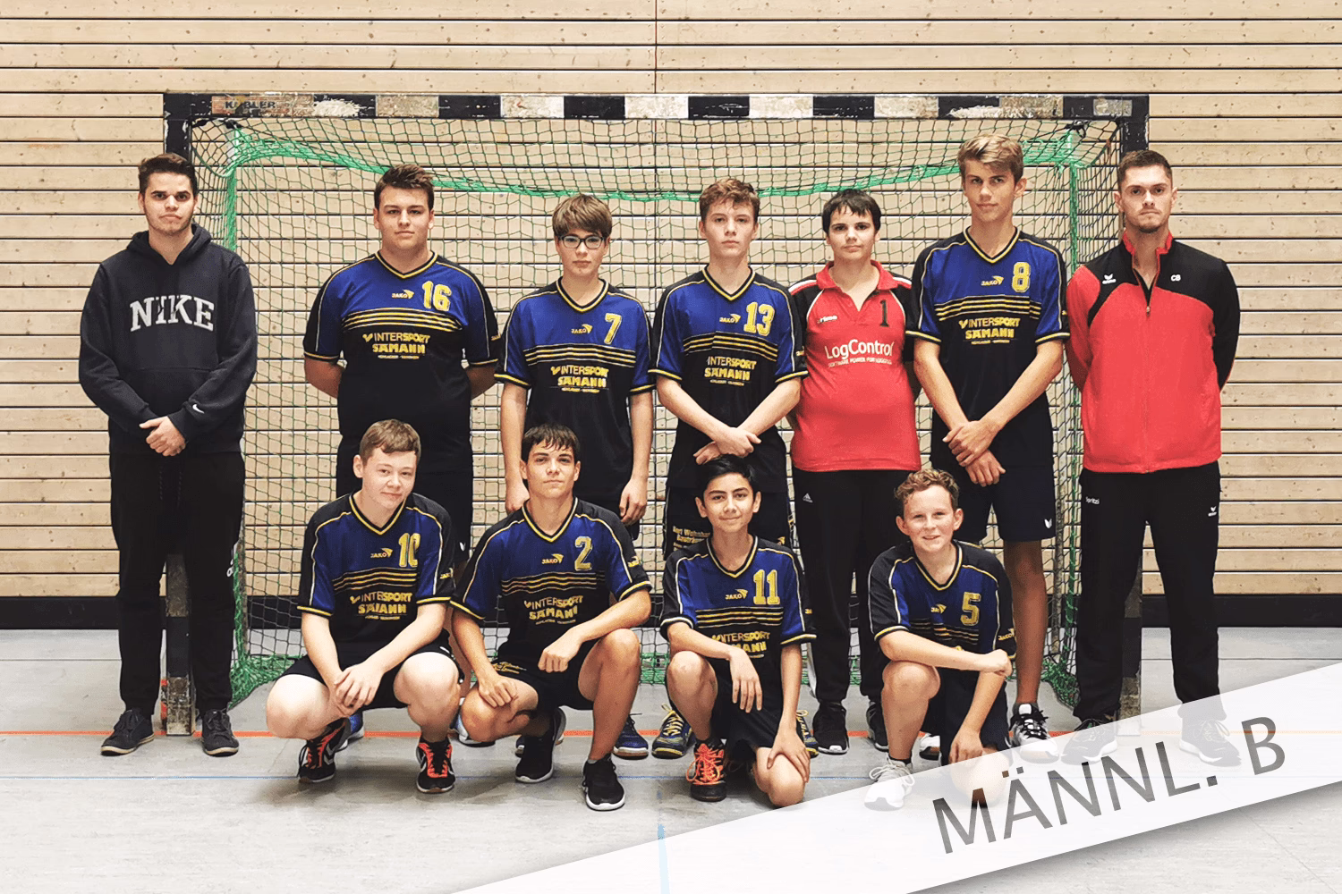 Mannschaftsfoto männlicher Handballspieler vor Tor, mehrere Spieler stehen und knien in Reihen, Sportbekleidung und Nummern sichtbar.