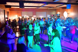 Feiernde Gäste in einer festlich beleuchteten Halle, stehen und sitzen an der Seite einer Bar; Stimmung mit farbigem Licht, Party-Atmosphäre.