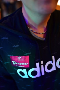 Nahaufnahme eines Halskettenanhängers mit Kettenring am Oberkörper, darüber bedruckter Sportpullover und Sponsoraufdruck.