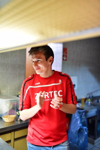 Sportler im roten Trikot im Innenraum; sitzt/steht am Tisch und gestikuliert im Gespräch. Background mit Sportveranstaltungs-Setup.