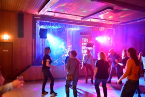 Festsaal mit Musikbühne, farbigem Licht, Band im Hintergrund und tanzenden Gästen im Vordergrund.