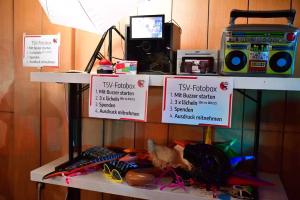 Fotokabine mit Bildschirm, Kamera und großer Anleitungstafel „TSV-Fotobox“; bereitgestelltes Equipment für Passfotos, inkl. Motiv- und Ablaufhinweisen.