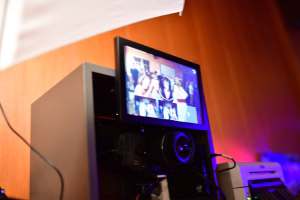Monitor mit Veranstaltungsvideo, um Raumpräsentation und Ablauf auf einer Bühne sichtbar zu machen. Kabel und beleuchtete Bühnenwand im Hintergrund.
