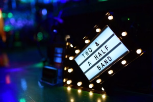 Leuchtendes Lichtspielband mit Schrift „TWO & HALF A… BUND“ auf dunkler Bühne, Fokus auf Event-Ansage und Stimmung.