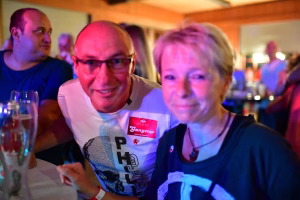 Zwei Personen sitzen dicht nebeneinander bei einer Feier im Restaurant, blau-rotes Licht; Blick nach vorne, angeregte Unterhaltung.