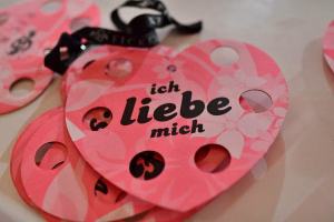 Rosa Glückwunschkarte mit gestanztem Muster und schwarzem Text „ich liebe dich mich“, dekoriert für eine Feier.