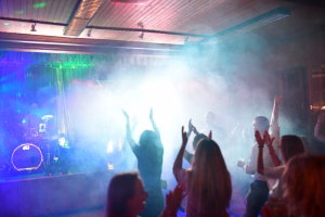 Rockkonzert mit Licht und Nebel: Musiker auf der Bühne, Publikum mit erhobenen Armen, als Blickfokus und Stimmungseindruck.